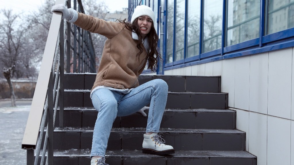 Young woman fallen on slippery stairs covered with ice outdoors