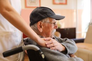 Caregiver supporting elderly man in wheelchair at nursing home facility to represent elder care and abuse prevention.