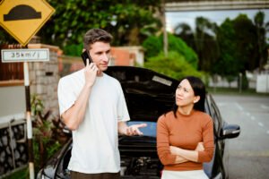 Driver speaking on the phone beside a disabled rental car after an accident in Illinois while a passenger looks concerned.