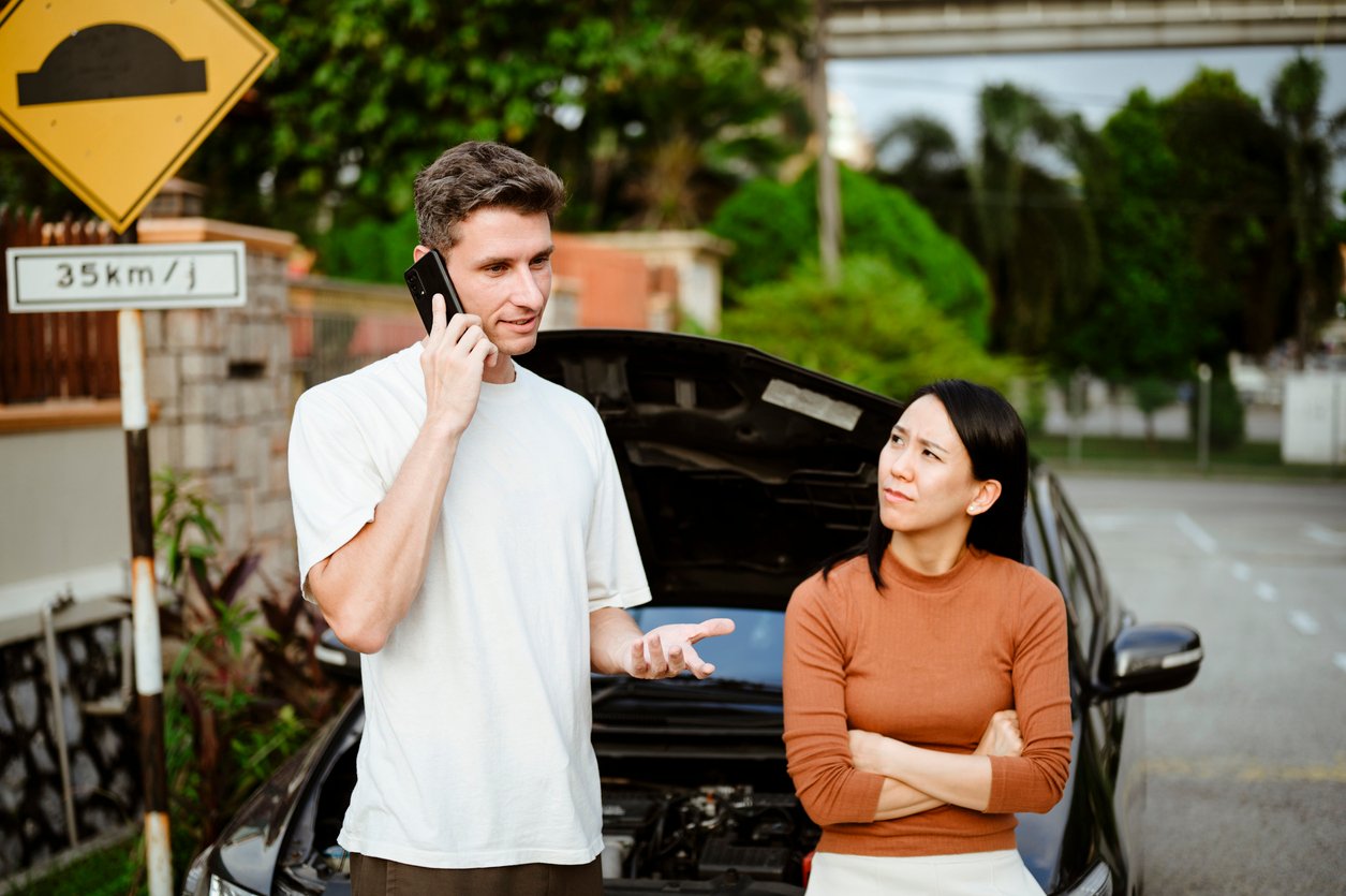 Driver speaking on the phone beside a disabled rental car after an accident in Illinois while a passenger looks concerned.